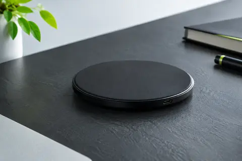 Pad de charge sans fil noir posé sur un bureau contemporain, avec son entrée micro USB visible