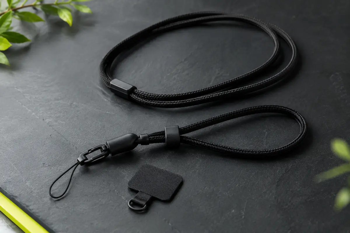 Cordon noir réglable pour téléphone avec patchs de fixation, posé sur un fond ardoise sobre