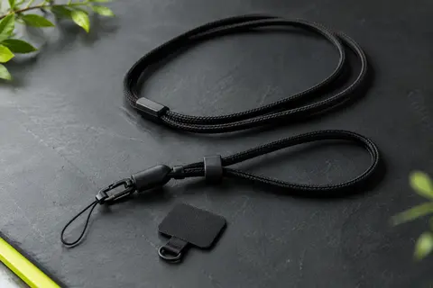 Cordon noir réglable pour téléphone avec patchs de fixation, posé sur un fond ardoise sobre
