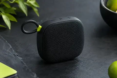 Enceinte Bluetooth noire compacte avec grille textile et boucle intégrée, présentée sur fond ardoise