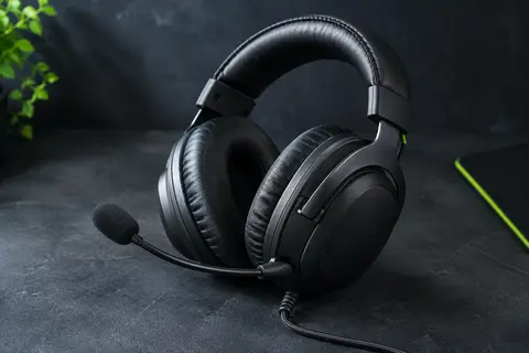 Casque gaming filaire noir avec oreillettes en similicuir, micro relevable et câble visible sur fond ardoise.