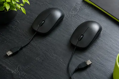 Deux souris Logitech M90 noires et filaires, présentées sur un fond ardoise avec leurs câbles USB visibles.