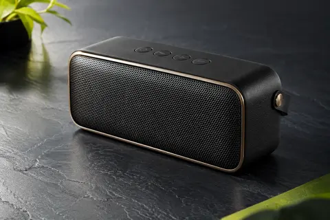 Enceinte portable noire et laiton avec grille métallique, présentée sur un fond ardoise.