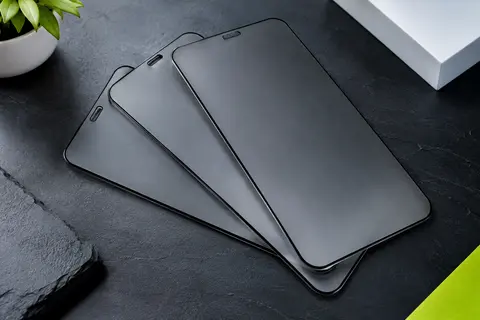 Lot de trois protections d’écran en verre trempé noir mat pour iPhone, posé sur un fond ardoise clair.