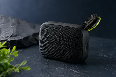 Enceinte Bluetooth portable noire avec sangle intégrée, photographiée sur un fond bleu nuit sobre.