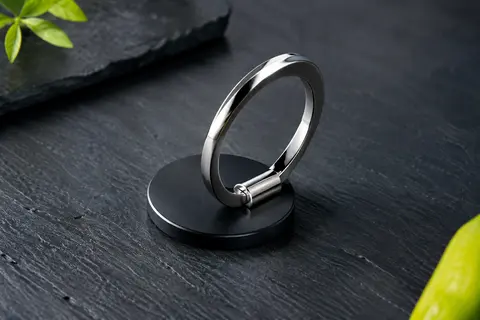 Anneau de support smartphone Syncwire noir, déplié sur un fond ardoise avec sa finition métallique visible.