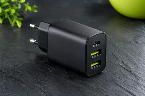 Chargeur secteur noir compact avec un port USB-C et deux ports USB-A sur fond ardoise.